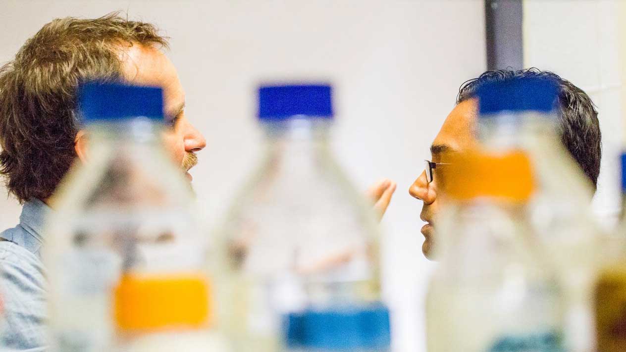two men in conversation behind colorful bottles of chemicals