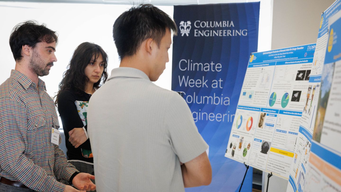 One attendee discusses research posters during a poster session at Columbia Engineering, while two attendees beside him look at the displays.