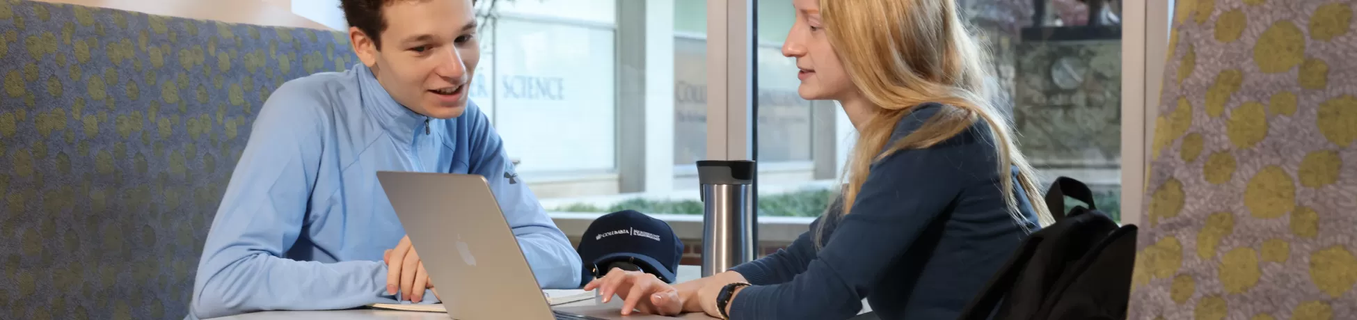 two people sitting across from each other in a booth, looking at a laptop screen together